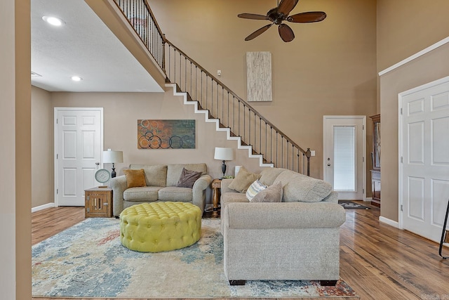 living area with stairs, a high ceiling, wood finished floors, and baseboards