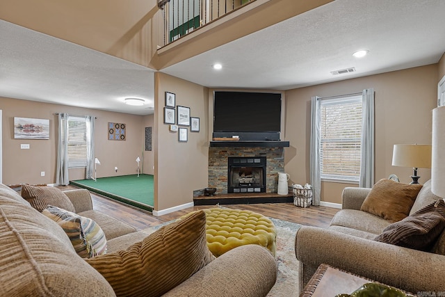 living room with a healthy amount of sunlight, visible vents, wood finished floors, and a stone fireplace