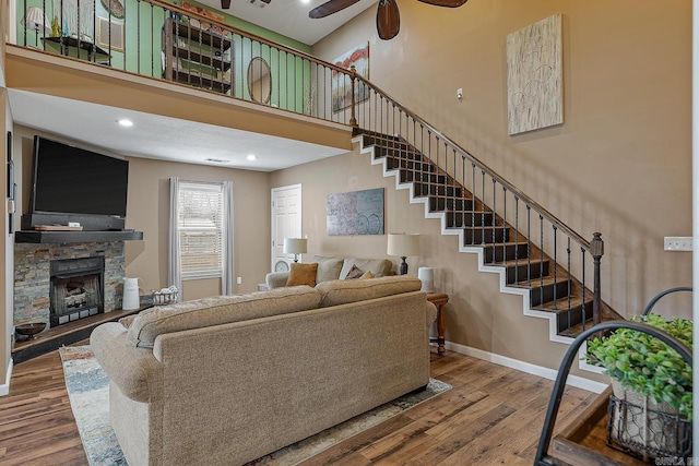 living area featuring stairway, baseboards, wood finished floors, and a stone fireplace