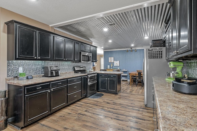 kitchen featuring stainless steel appliances, dark cabinetry, wood finished floors, and decorative backsplash