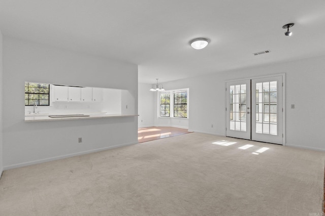 unfurnished living room featuring a chandelier, french doors, and light colored carpet