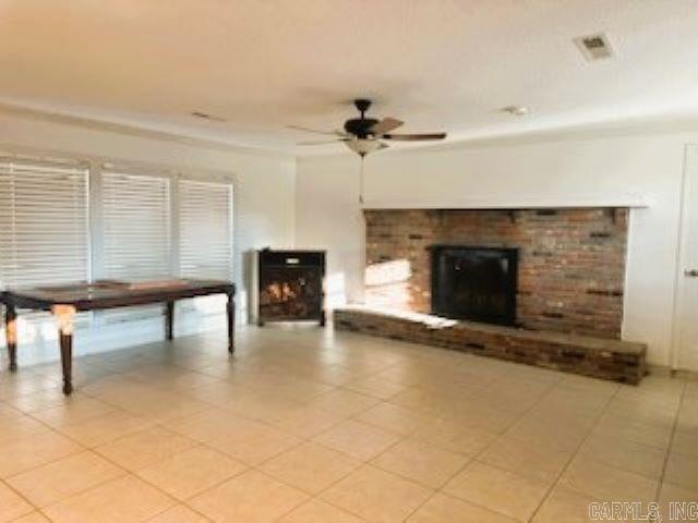 unfurnished living room featuring a fireplace, ceiling fan, and light tile patterned flooring