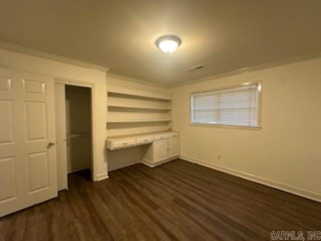 unfurnished bedroom with a closet, dark wood-type flooring, and ornamental molding