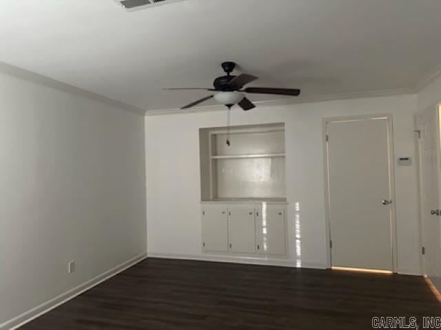 unfurnished room featuring crown molding, built in features, ceiling fan, and dark wood-type flooring