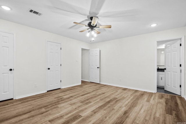 unfurnished bedroom featuring ensuite bathroom, ceiling fan, light hardwood / wood-style floors, and two closets