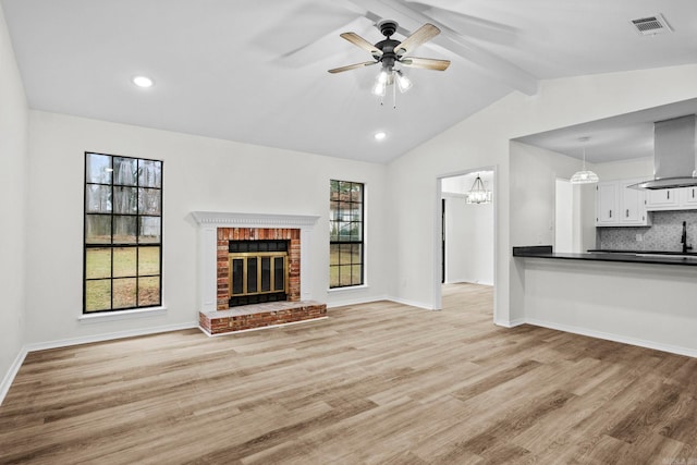 unfurnished living room with vaulted ceiling with beams, light hardwood / wood-style floors, ceiling fan with notable chandelier, and a brick fireplace