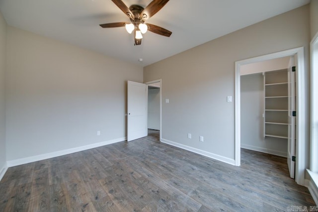 unfurnished bedroom featuring a walk in closet, a closet, ceiling fan, and dark wood-type flooring