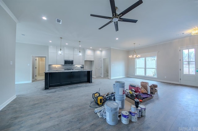 interior space featuring ceiling fan with notable chandelier, a kitchen island with sink, crown molding, white cabinetry, and hanging light fixtures