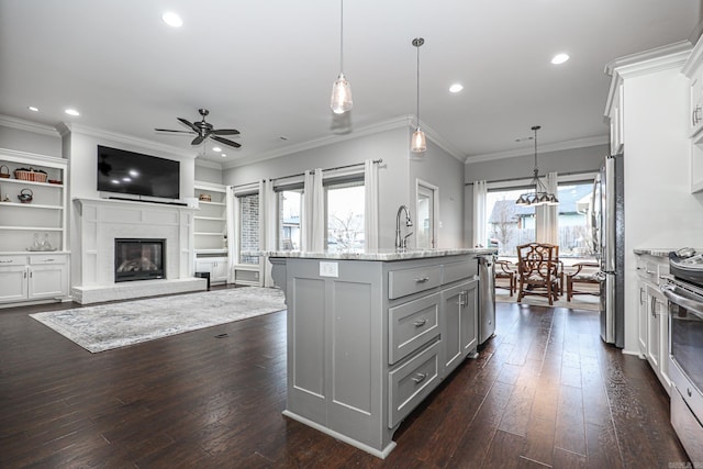 kitchen with decorative light fixtures, ceiling fan, a kitchen island with sink, and appliances with stainless steel finishes