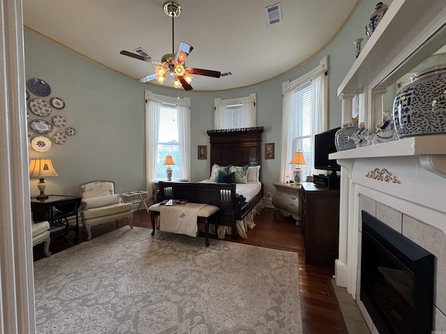 bedroom with a tile fireplace, dark hardwood / wood-style floors, and ceiling fan