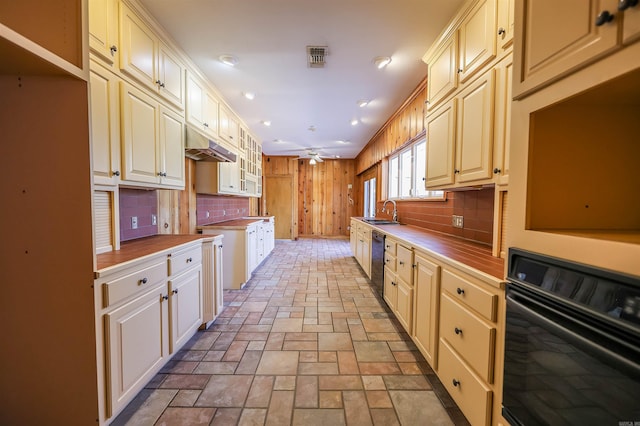 kitchen featuring sink, decorative backsplash, wooden walls, and black appliances