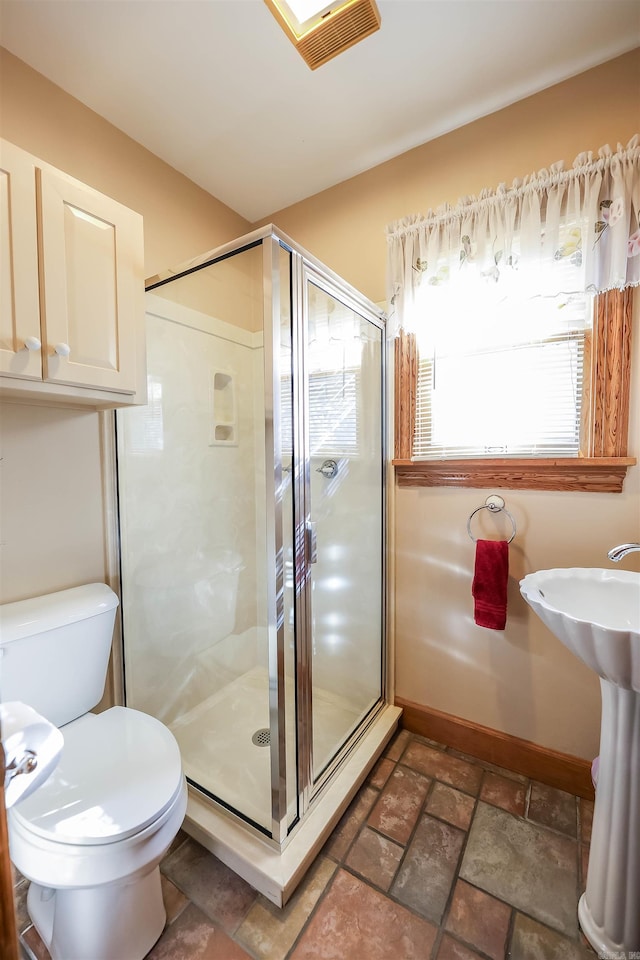 bathroom featuring sink, a shower with door, and toilet