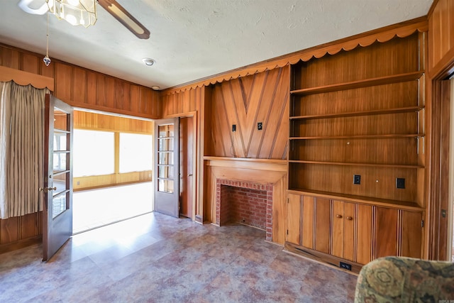 unfurnished living room with a brick fireplace, ceiling fan, and wood walls