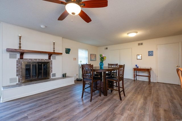 dining room featuring a tile fireplace, wood-type flooring, a textured ceiling, and ceiling fan