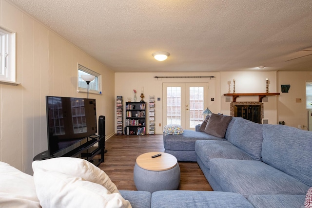 living room with french doors, a textured ceiling, dark hardwood / wood-style floors, and a brick fireplace