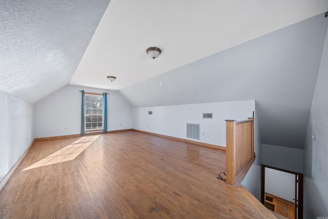 bonus room featuring a textured ceiling, hardwood / wood-style flooring, and vaulted ceiling