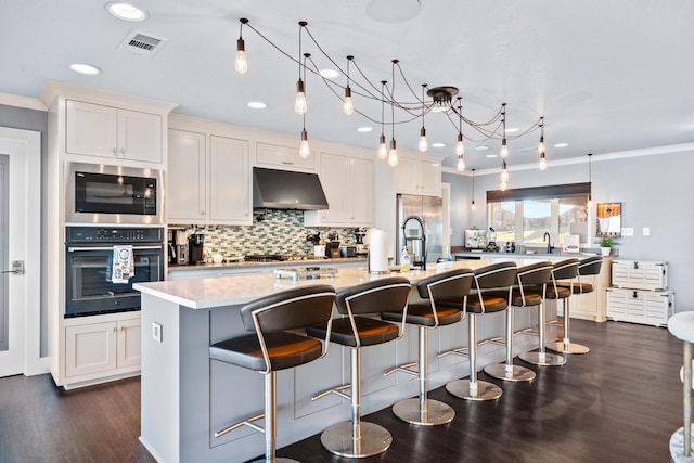 kitchen featuring stainless steel appliances, an island with sink, a kitchen bar, decorative backsplash, and white cabinets