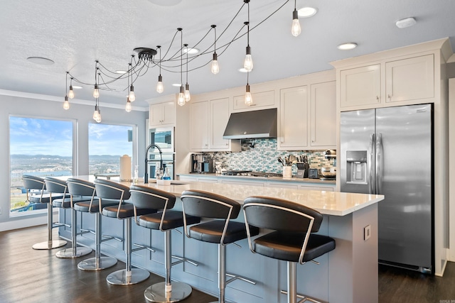 kitchen with white cabinets, pendant lighting, stainless steel appliances, and an island with sink