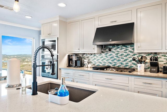 kitchen featuring light stone countertops, backsplash, crown molding, sink, and white cabinetry