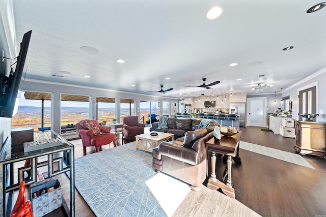 living room with dark wood-type flooring, ceiling fan, and crown molding