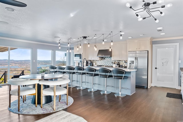 kitchen featuring white cabinetry, stainless steel appliances, decorative light fixtures, a kitchen bar, and a center island with sink