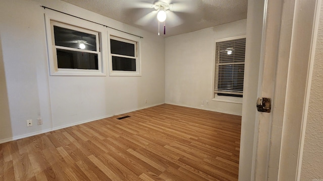 unfurnished room with a textured ceiling, light wood-type flooring, and ceiling fan