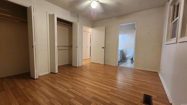 unfurnished bedroom featuring ensuite bath, a textured ceiling, ceiling fan, light hardwood / wood-style floors, and multiple closets