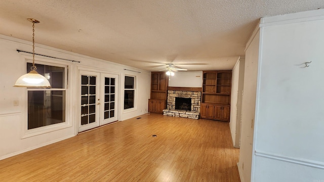 unfurnished living room featuring a stone fireplace, built in shelves, ceiling fan, a textured ceiling, and wood-type flooring