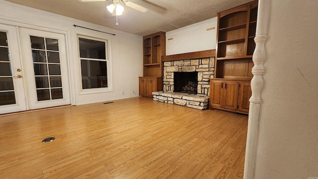 unfurnished living room featuring french doors, a stone fireplace, ceiling fan, built in features, and a textured ceiling