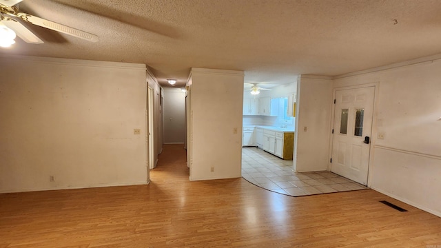 empty room with ceiling fan, light hardwood / wood-style flooring, a textured ceiling, and ornamental molding