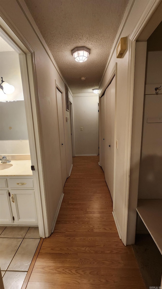 hall with sink, light hardwood / wood-style floors, and a textured ceiling