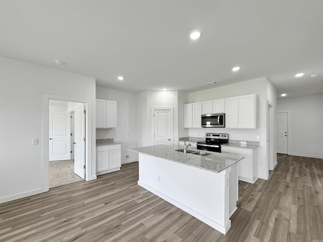 kitchen with sink, an island with sink, appliances with stainless steel finishes, light stone counters, and white cabinetry