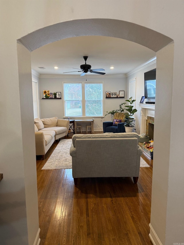 living room featuring ceiling fan, dark hardwood / wood-style flooring, ornamental molding, and a tile fireplace