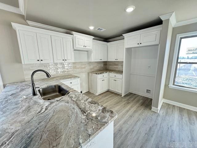 kitchen featuring white cabinets, light stone countertops, crown molding, and sink