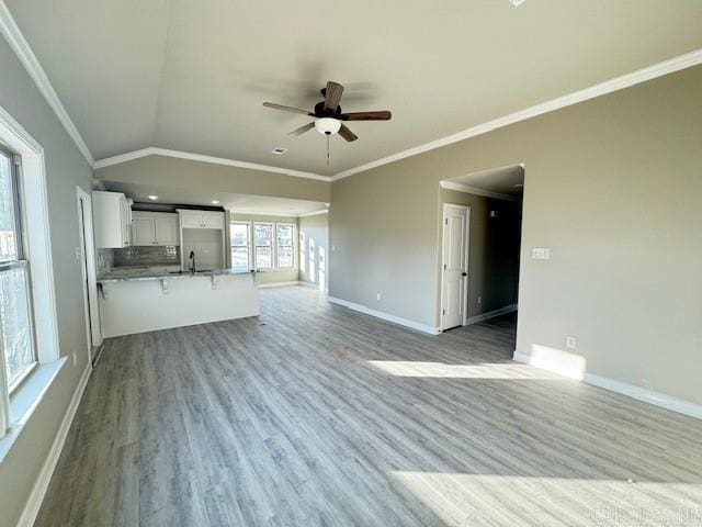 unfurnished living room with ceiling fan, sink, crown molding, light hardwood / wood-style floors, and lofted ceiling