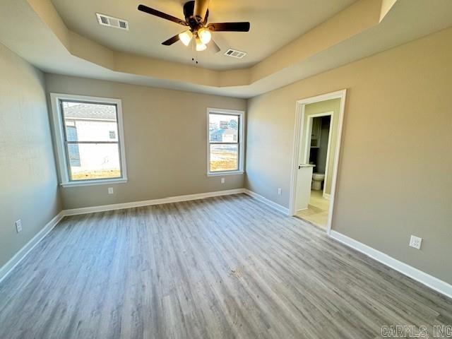 unfurnished room featuring a raised ceiling, ceiling fan, and light hardwood / wood-style floors