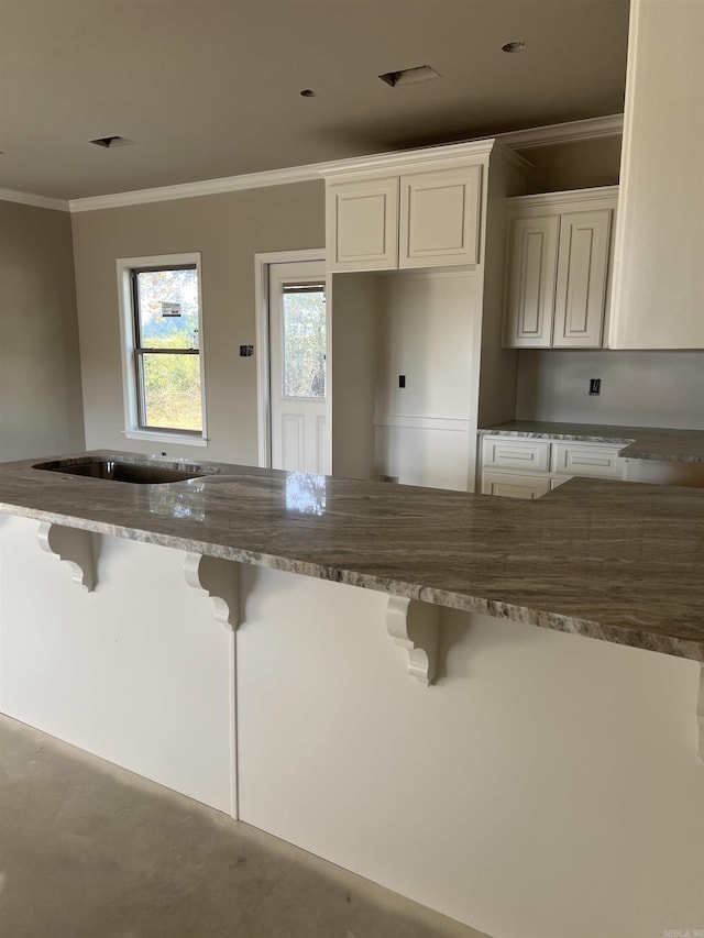 kitchen with white cabinets, a kitchen bar, and ornamental molding