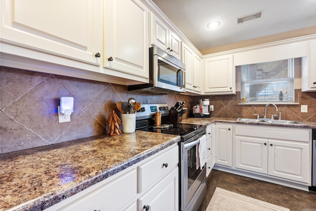 kitchen featuring decorative backsplash, dark stone counters, stainless steel appliances, sink, and white cabinetry