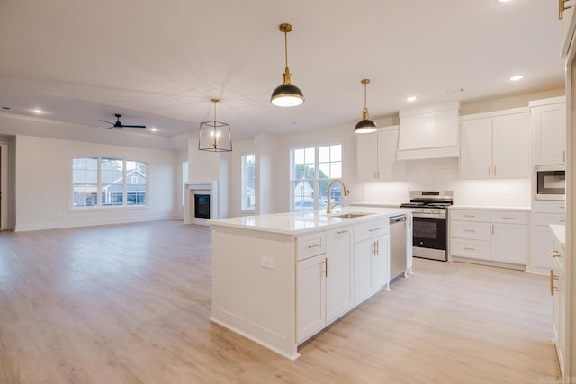 kitchen with sink, custom range hood, an island with sink, white cabinetry, and stainless steel appliances