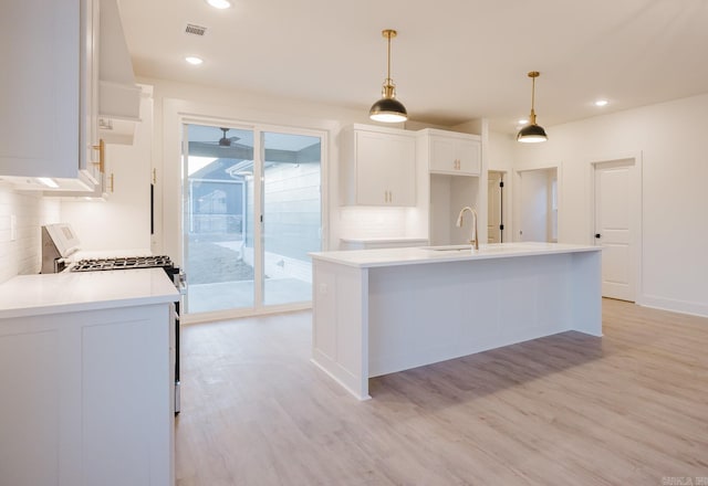 kitchen featuring backsplash, light wood-type flooring, decorative light fixtures, white cabinets, and range