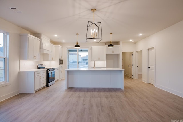 kitchen featuring white cabinets, stainless steel appliances, hanging light fixtures, and a kitchen island with sink