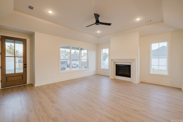 unfurnished living room featuring a tray ceiling, ceiling fan, and light hardwood / wood-style flooring