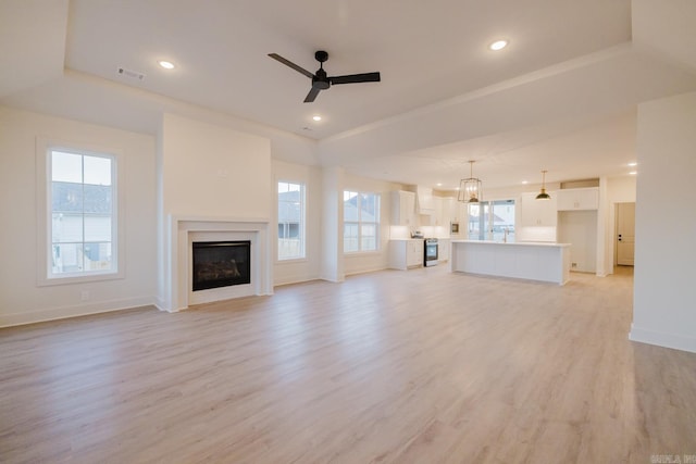 unfurnished living room with ceiling fan, a raised ceiling, and light wood-type flooring