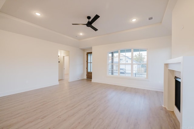 unfurnished living room with a tray ceiling, ceiling fan, and light hardwood / wood-style flooring