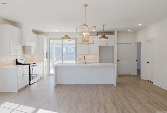 kitchen featuring backsplash, gas range, pendant lighting, a center island with sink, and white cabinetry