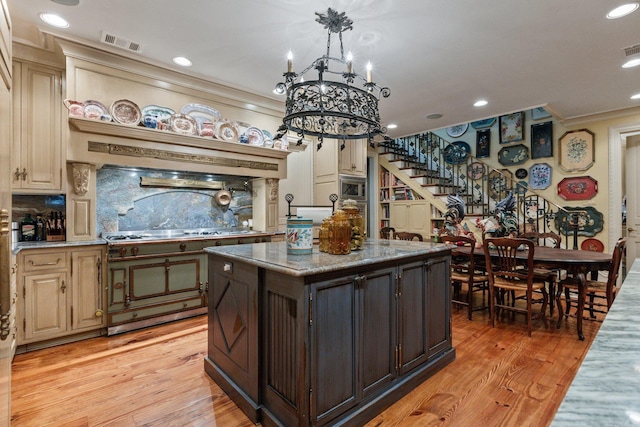 bar featuring light hardwood / wood-style flooring, range with gas cooktop, a notable chandelier, cream cabinetry, and decorative backsplash