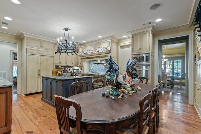 dining area with light wood-type flooring, ornamental molding, and a chandelier