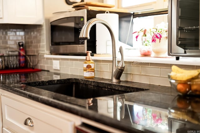 interior details with white cabinets, backsplash, dark stone countertops, and sink