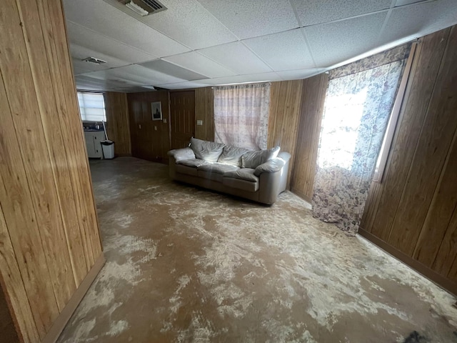 living room featuring a wealth of natural light, wooden walls, a drop ceiling, and concrete flooring