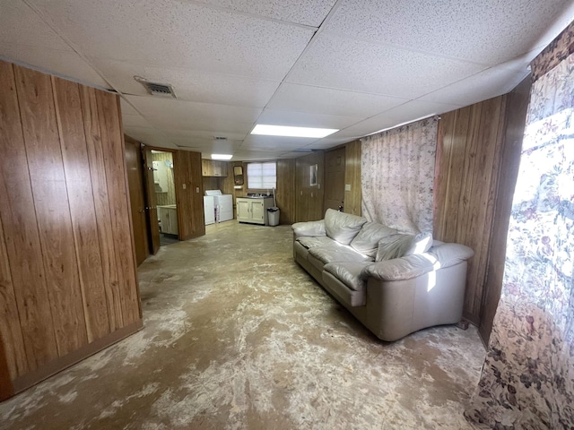 interior space featuring separate washer and dryer, a drop ceiling, and wood walls